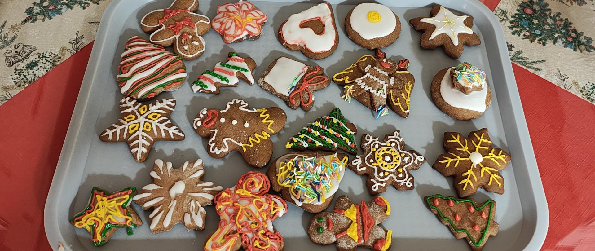 Na szarej tacy leży kilkanaście udekorowanych kolorowymi lukrami i posypkami pierników