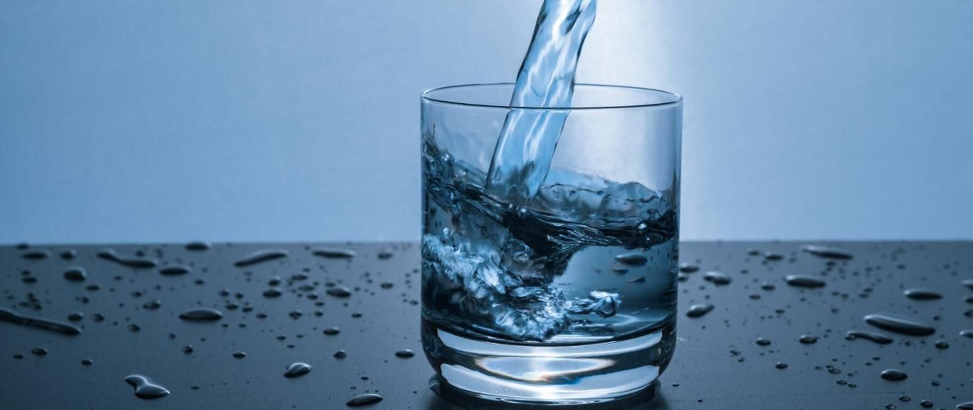 Obrazek przedstawiający szklankę wody, do której wlewana jest woda