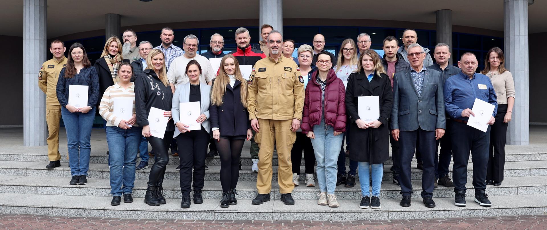Pamiątkowe zdjęcie grupowe uczestników szkolenia inspektorów ochrony przeciwpożarowej (25 osób) w towarzystwie Zastępcy Komendanta Centralnej Szkoły PSP, kobiety orz funkcjonariusza CS PSP