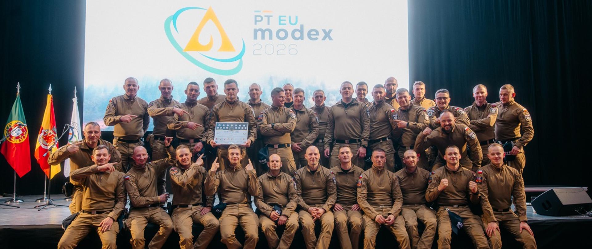 Grupa strażaków GFFF Poland pozuje na scenie do pamiątkowego zdjęcia podczas wydarzenia związanego z ćwiczeniami PT EU MODEX 2026.