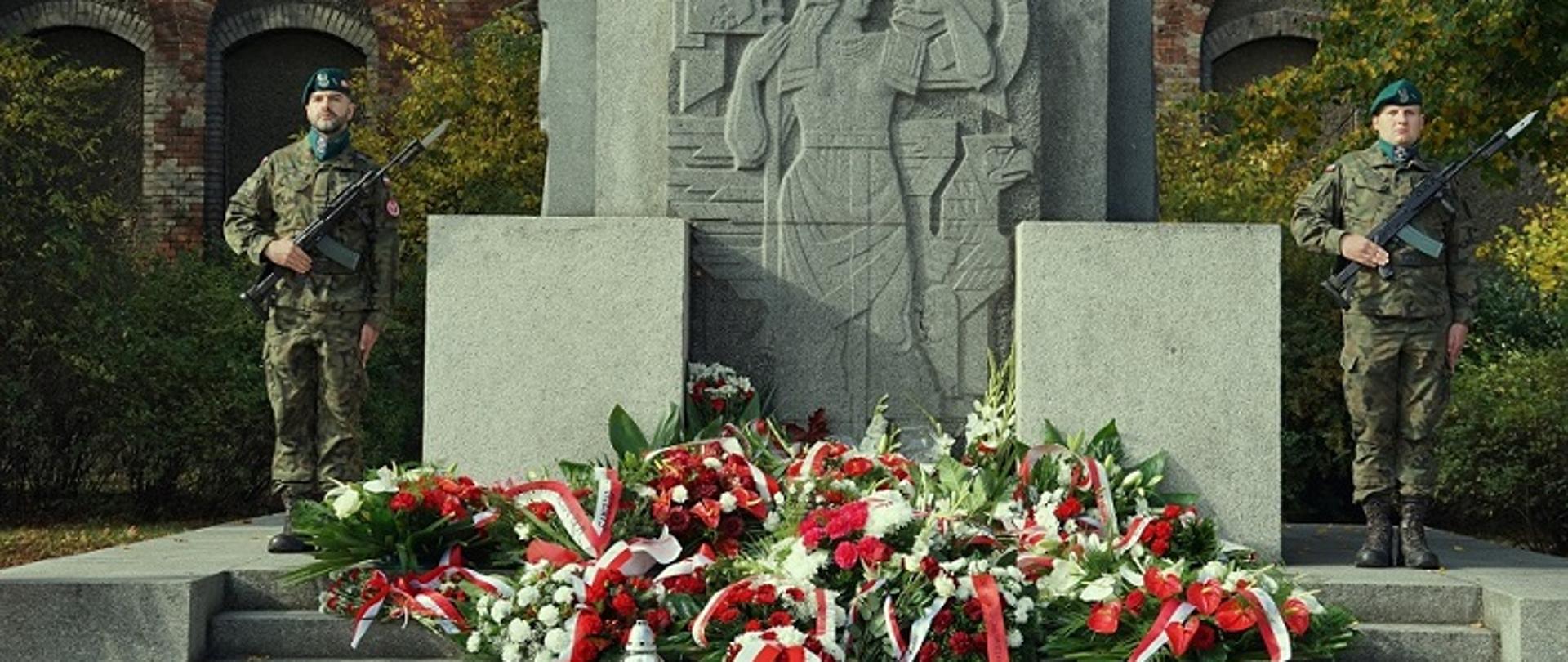 pomnik przy którym stoi dwóch żołnierzy, warta, prxzed pomnikiem wiązanki biało czerwone