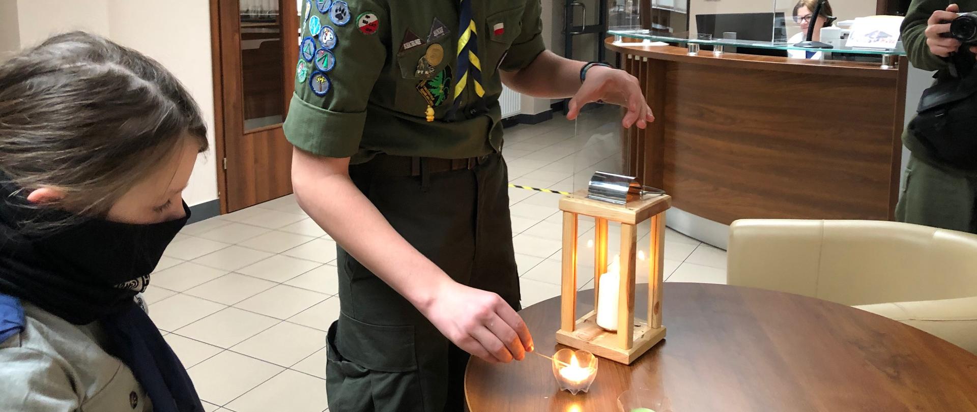 Harcerz zapalaną zapałką odpala małą świeczkę dla KM PSP Nowy Sącz.