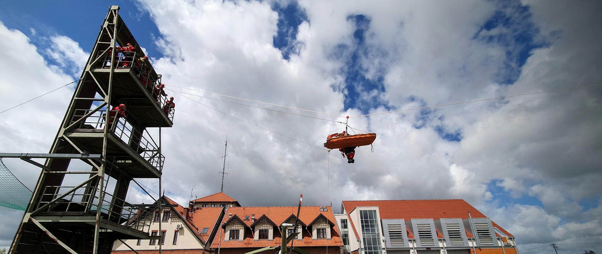 Zdjęcie przedstawia ewakuację poszkodowanego przez ratownika wysokościowego (wszyscy odpowiedni zabezpieczeni) metodą liny kierunkowej do Zespołu Ratownictwa Medycznego