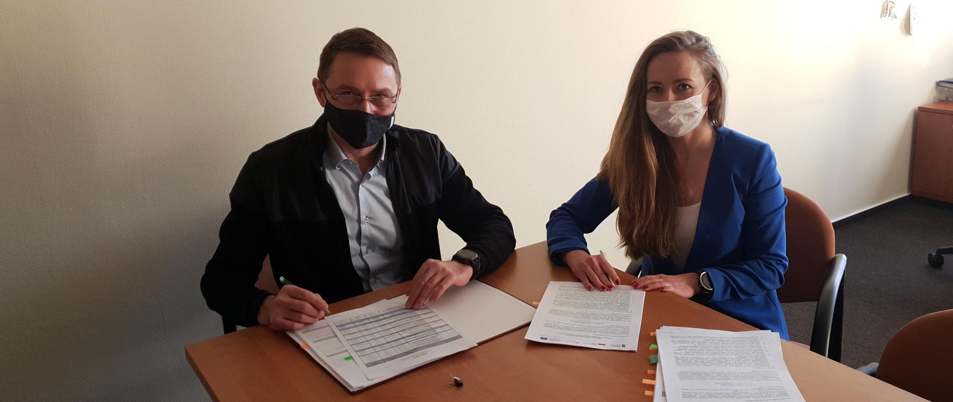 Ładnie ubrani kobieta i mężczyzna siedzą przy stole i podpisują dokumenty