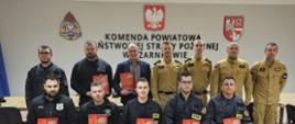 Pamiątkowe zdjęcie uczestników egzaminu recertyfikacyjnego z kwalifikowanej pierwszej pomocy dla druhów OSP, przeprowadzonego w Komendzie Powiatowej PSP w Czarnkowie – w tle godło RP i logotyp komendy.