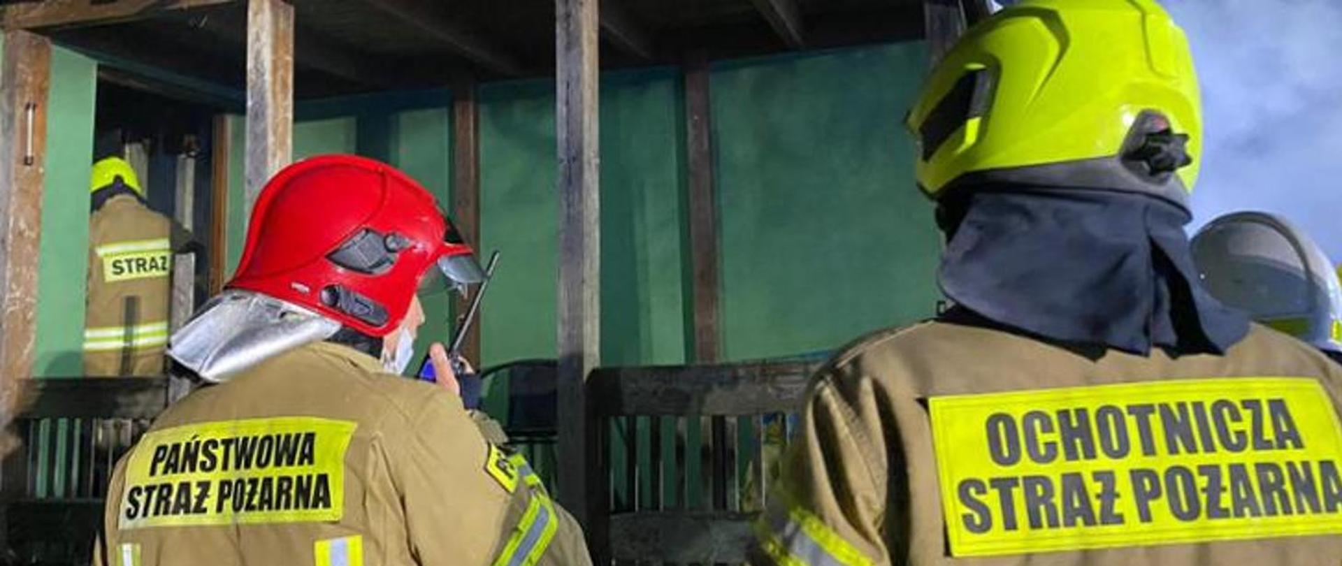 Na zdjęciu widać trzech strażaków odwróconych plecami jeden z nich trzyma w dłoni krótkofalówkę.