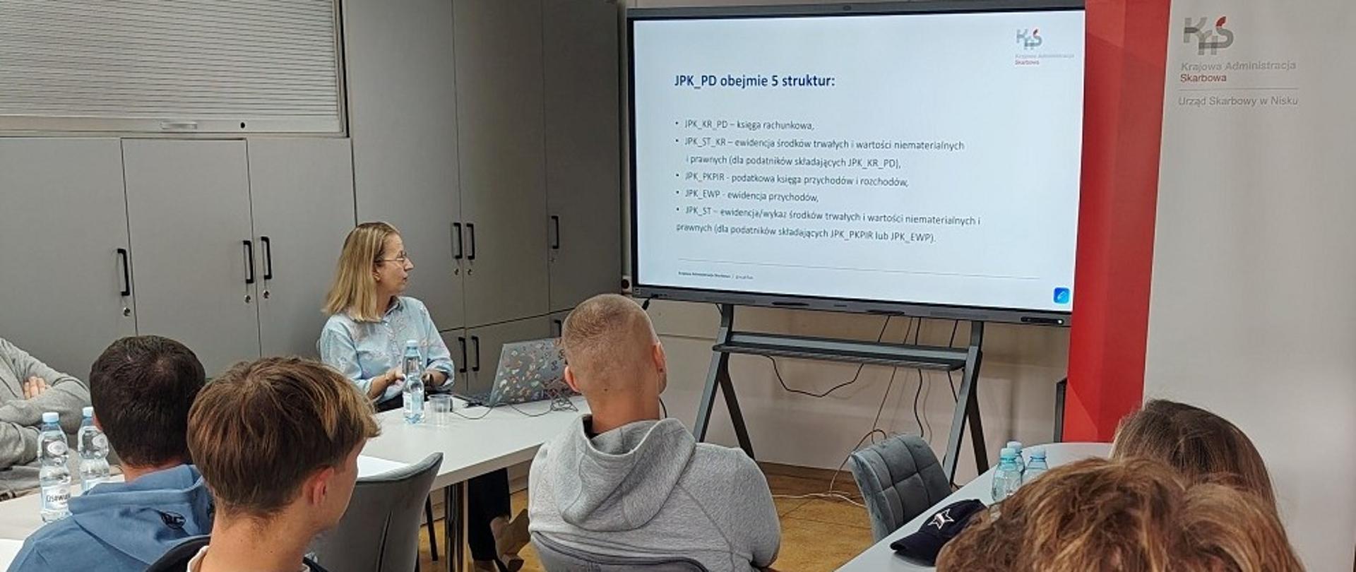 Uczestnicy siedzą w sali. Wśród nich jest ekspertka. Na ekranie wyświetlana jest prezentacja.