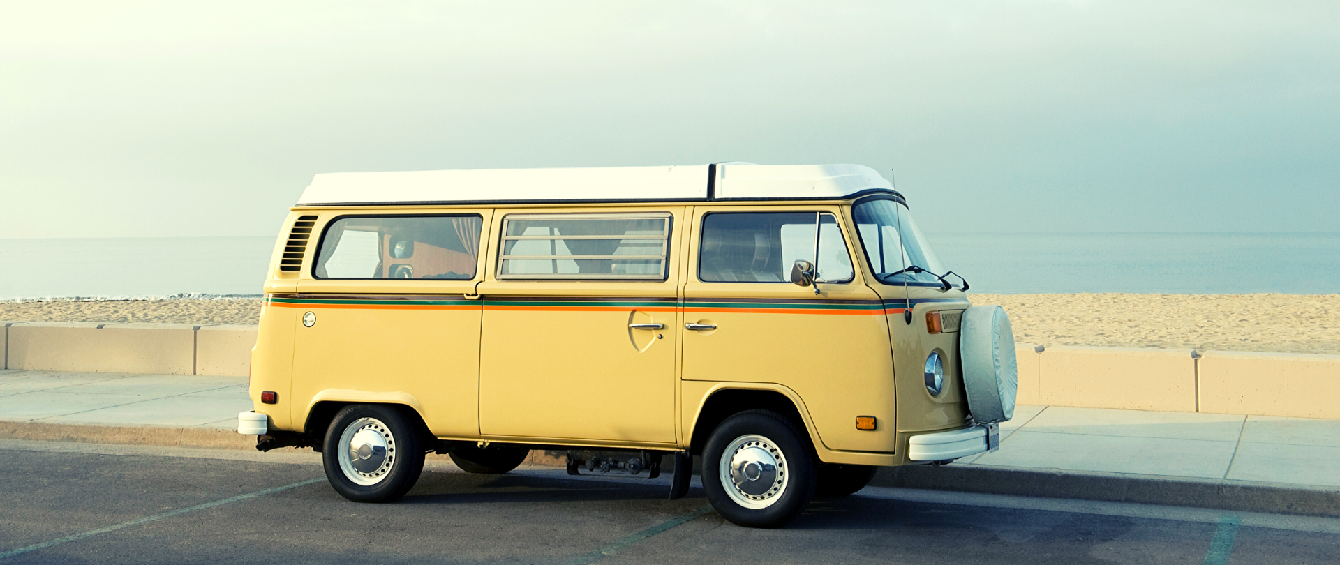 Żółty kamper - Volkswagen T2 - podczas postoju na ulicy, w tle morze.