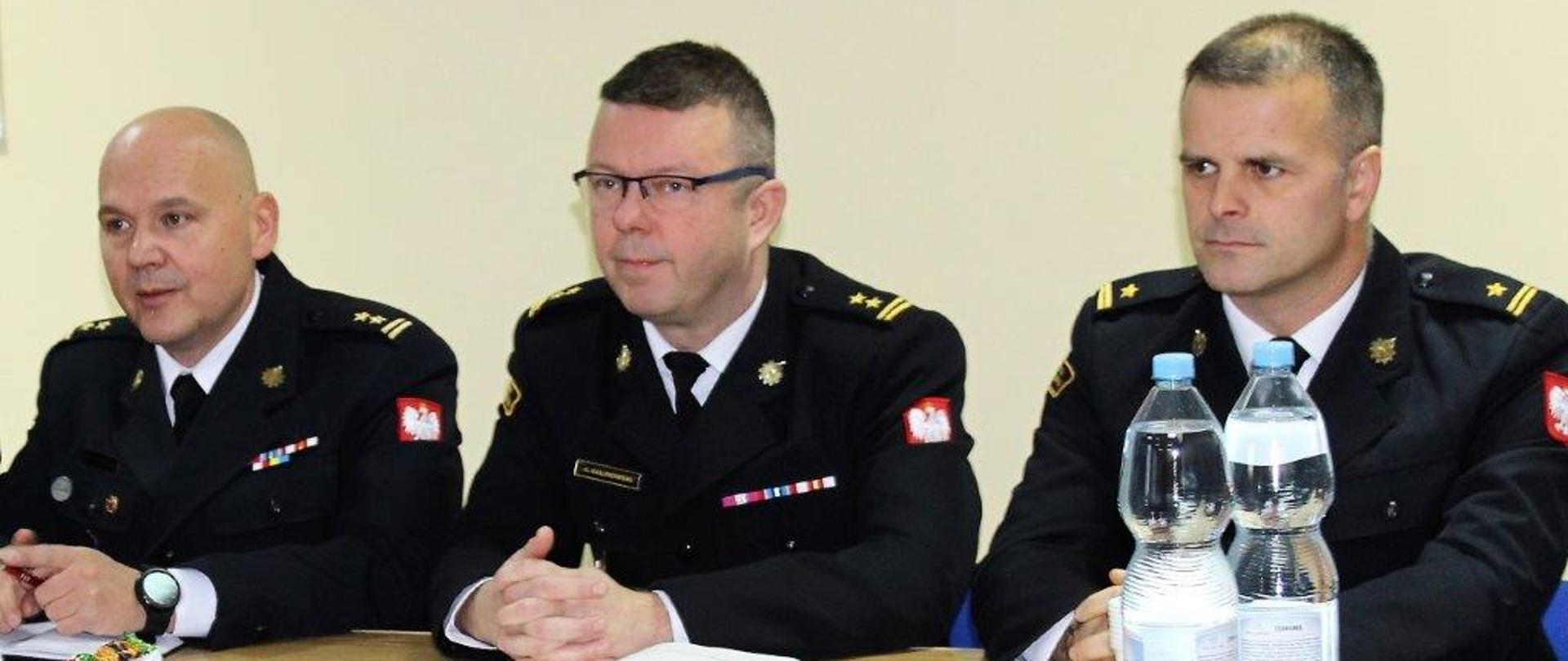 Trzech funkcjonariuszy ubranych w mundury wyjściowe siedzi na stołem