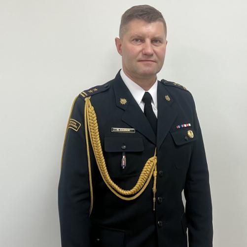 Zdjęcie przedstawia funkcjonariusza ubranego w mundur galowy ze złotym sznurem.