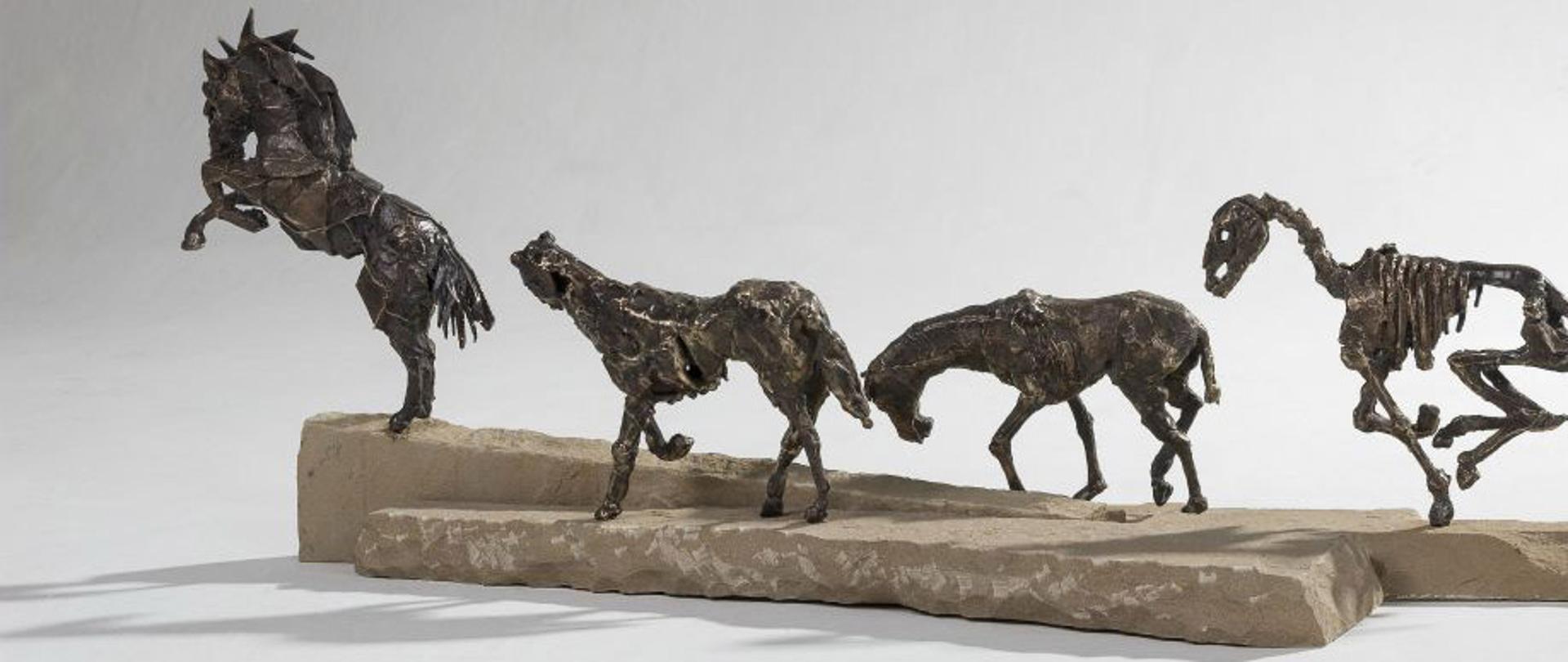 Zdjęcie przedstawia grupę czterech koni. Odlewy z mosiądzu ustawione na płaskim kamieniu
