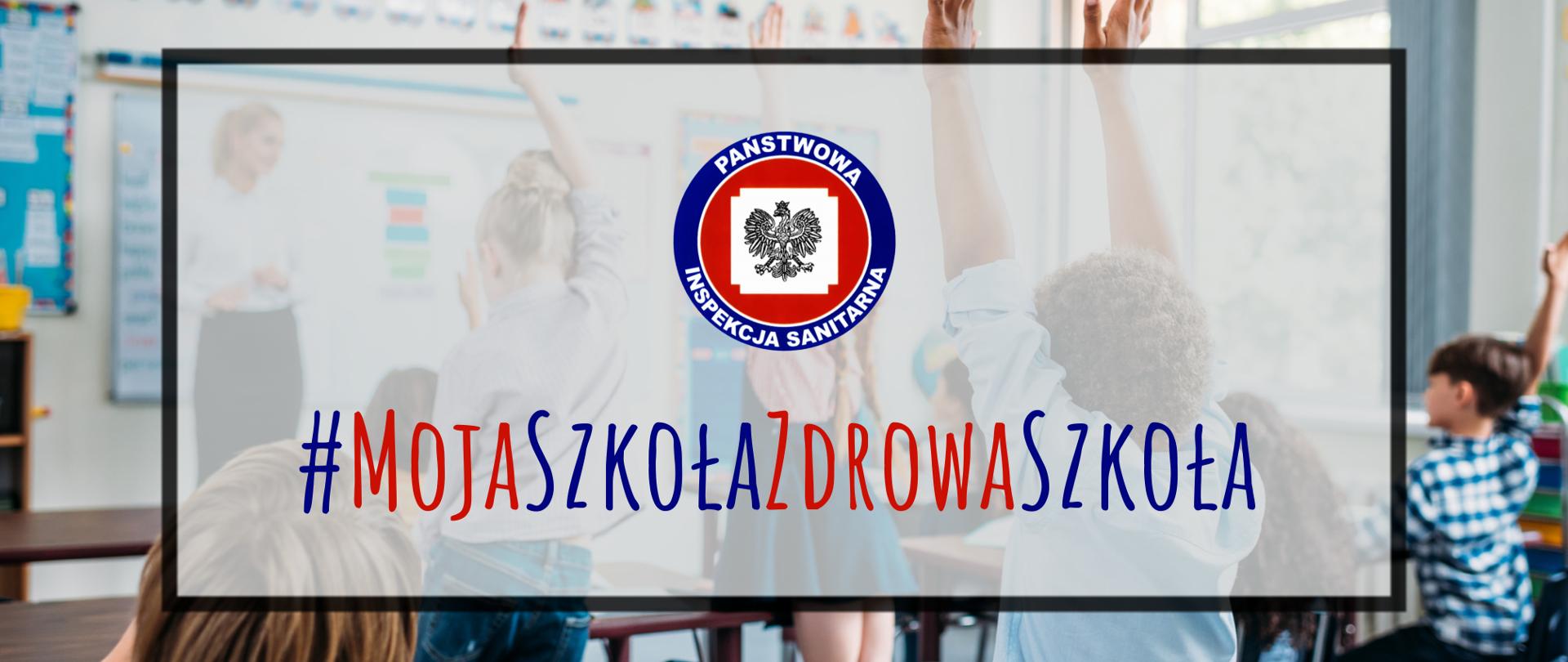 Na zdjęciu jest logo Państwowej Inspekcji Sanitarnej. Poniżej jest napis #MojaSzkołaZdrowaSzkoła. W tle widać uczniów oraz nauczycielkę podczas zajęć.