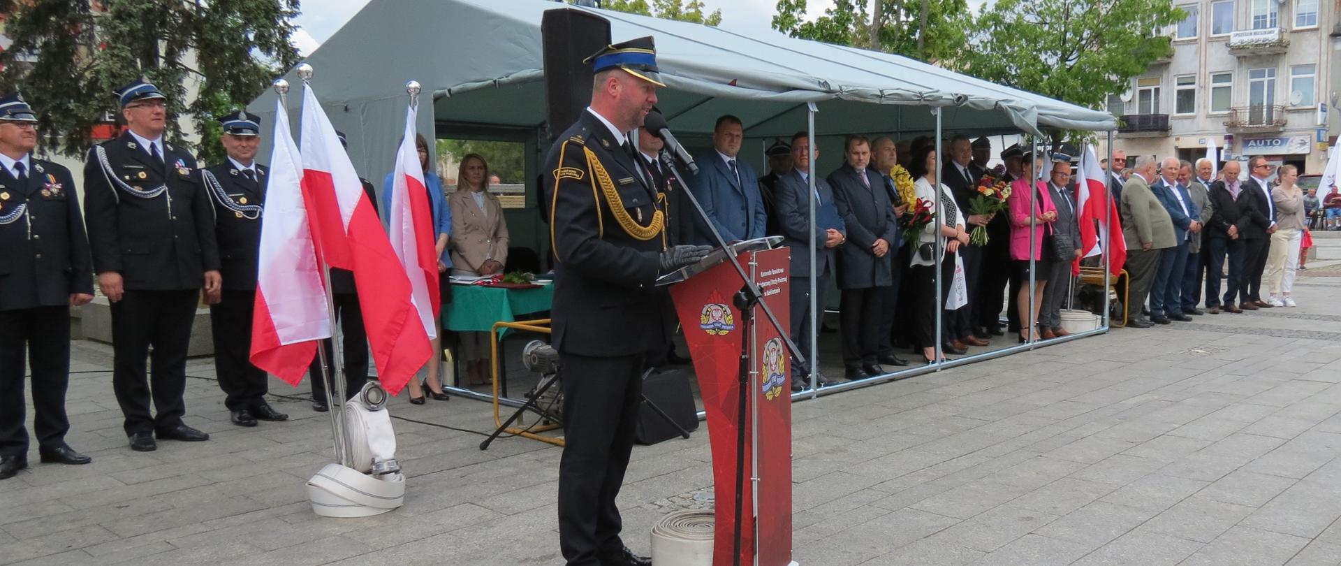 na zdjęciu komendant straży pożarnej przemawiający do strażaków z okazji dnia strażaka oraz 30 lecia straży pożarnej w tle pod namiotem zaproszeni goście
