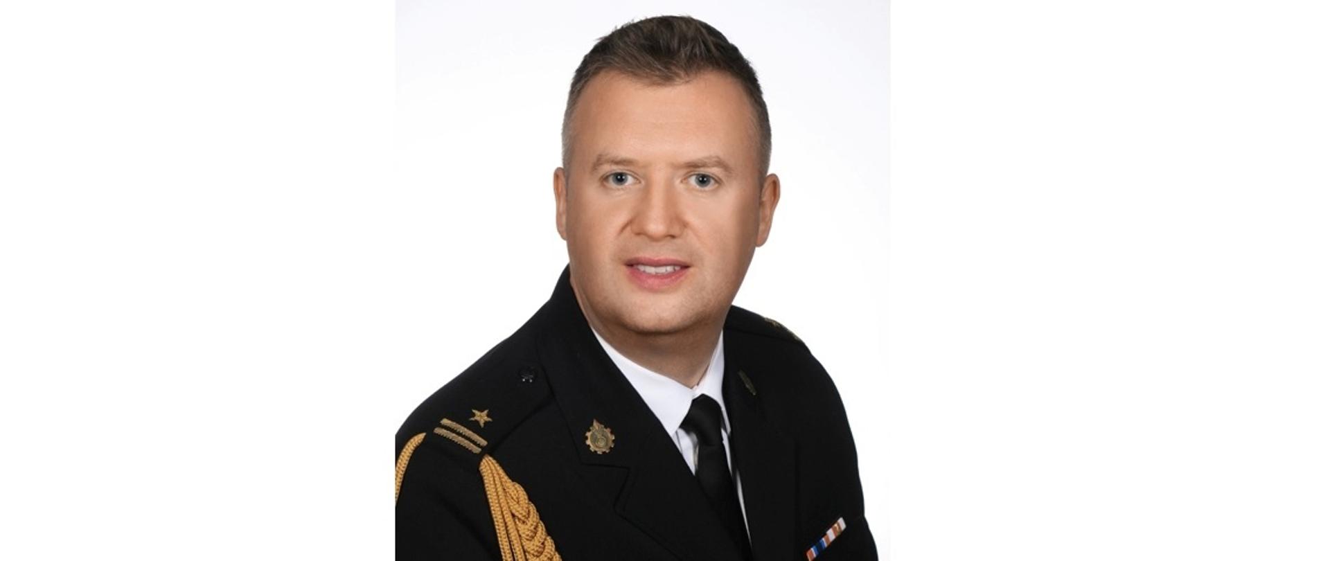 zdjęcie przedstawia Komendanta Powiatowego PSP w Bełchatowie mł. bryg. Adama Pstrokońskiego w mundurze wyjściowym na białym tle.