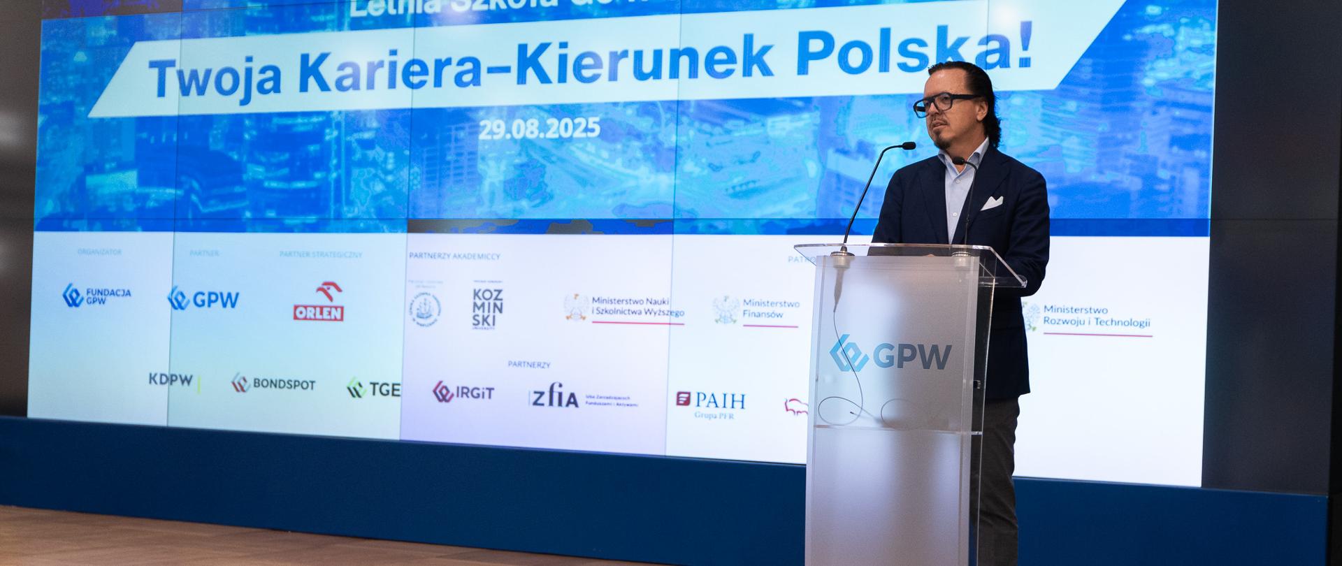Minister Wojciech Balczun stoi za mównicą. W tle ekran z napisem Letnia Szkoła Go4Poland "Twoja Kariera - Kierunek Polska!".
