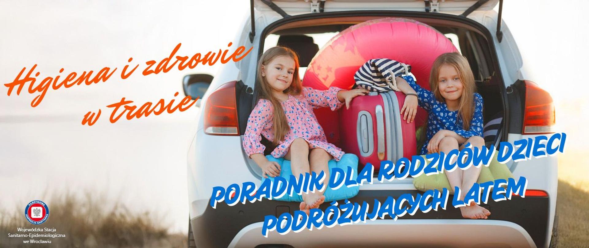 Dwoje dzieci siedzących w otwartym bagażniku samochodu typu SUV. Pomiędzy nimi kolorowe walizki