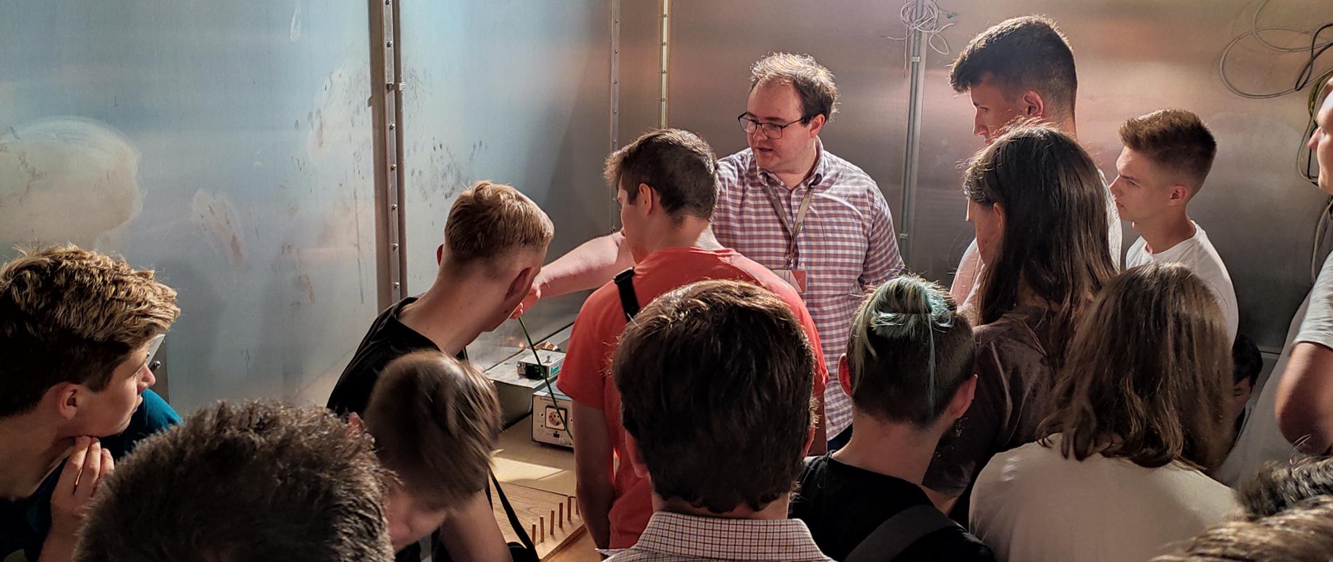 Uczniowie technikum z Łochowa podczas wizyty w Instytucie Łączności słuchają wykładu eksperta Instytutu wewnątrz klatki Faradaya.