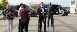 Na pierwszym planie (od lewej): Minister Edukacji i Nauki Przemysław Czarnek i Główny Inspektor Transportu Drogowego Alvin Gajadhur stoją przed mikrofonami. O rozpoczętych kontrolach autokarów turystycznych mówi Minister Edukacji i Nauki Przemysław Czarnek. W tle: oznakowany furgon Inspekcji Transportu Drogowego i Stadion Narodowy w Warszawie.