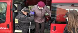 Strażak pomaga kobiecie wysiąść z samochodu pożarniczego typu BUS.