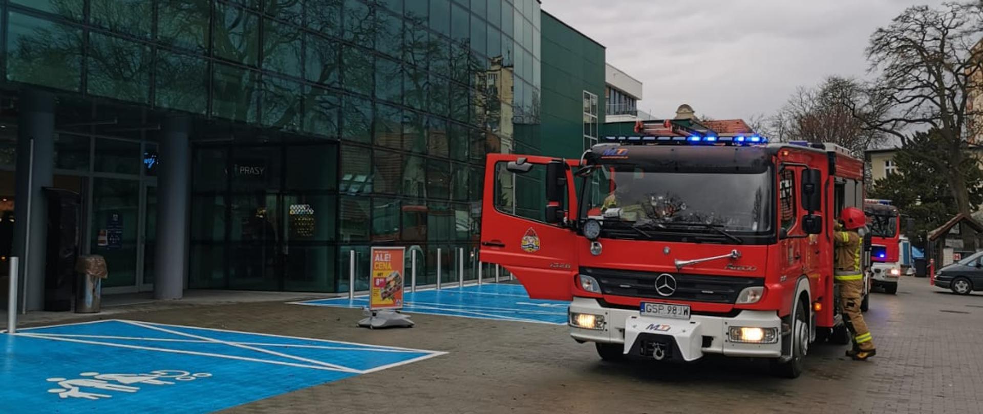 Trzy samochody ratowniczo gaśnicze stojące na sygnałach świetlnych przed wejściem do sklepu ALDI