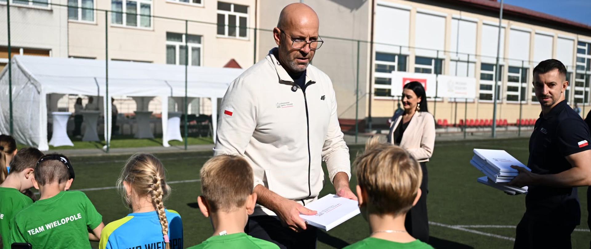 Zdjęcie przedstawia ministra sportu i dzieci na boisku