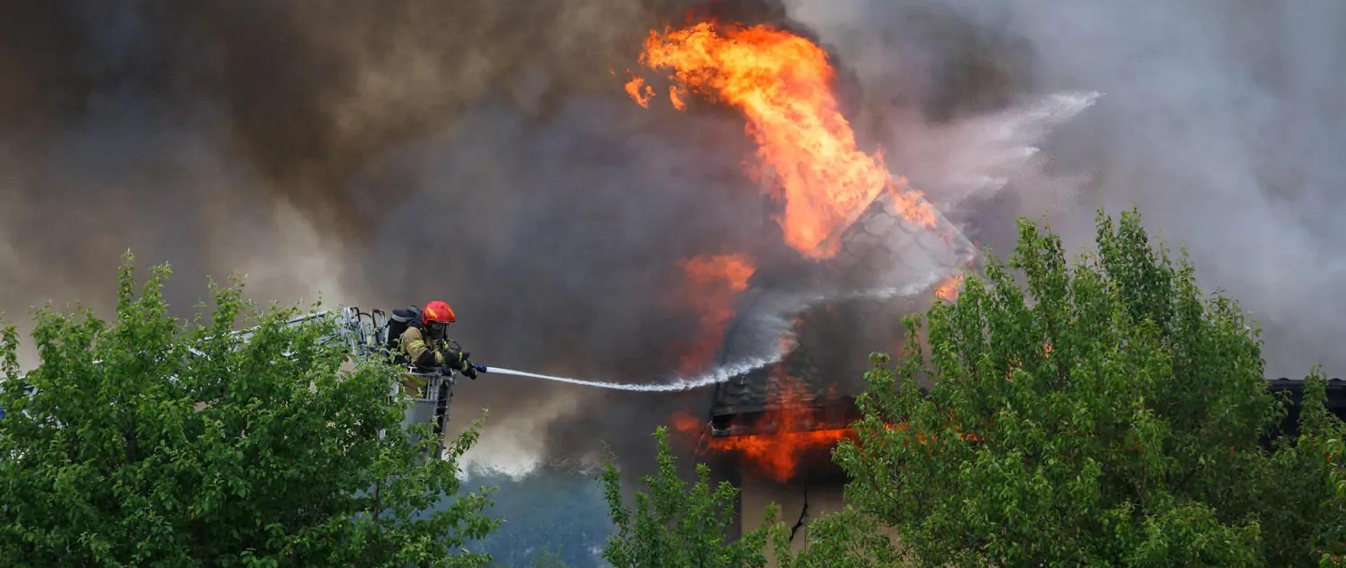Pożar stolarni. Strażak będący w koszu drabiny pożarniczej w trakcie gaszenia pożaru