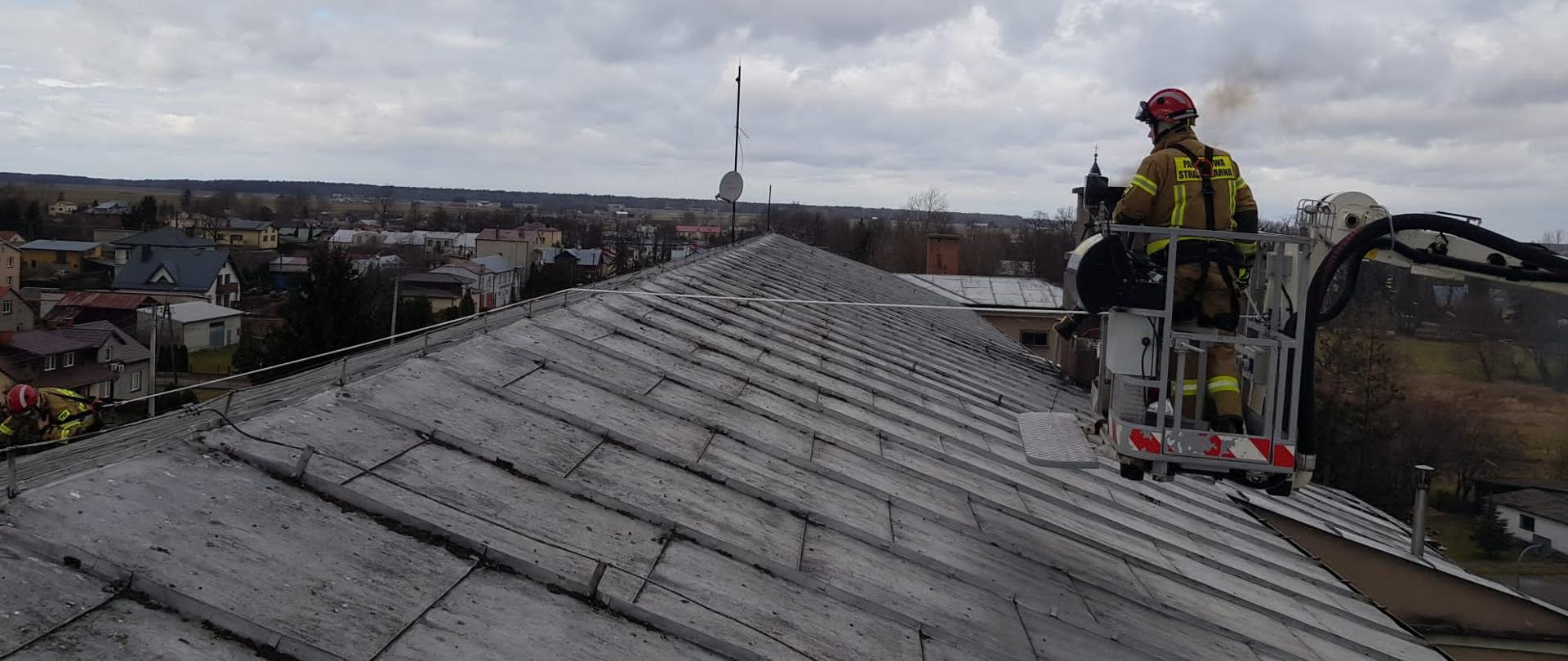 Sokołowscy strażacy w walce z usuwaniem skutków silnego wiatru 19 lutego 2022 r. - na zdjęciu uszkodzony dach, strażacy naprawiają dach przy pomocy podnośnika