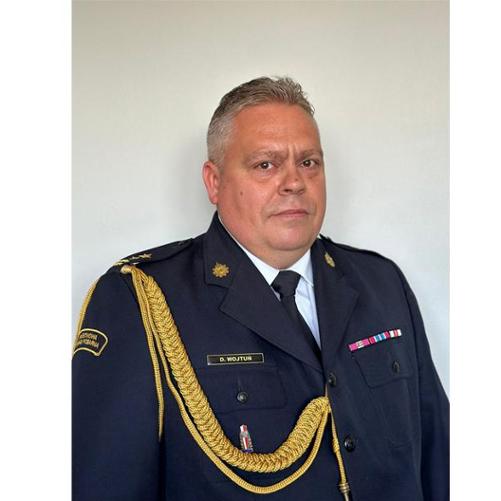 Zdjęcie portretowe Komendanta Powiatowego Państwowej Straży Pożarnej w Krośnie Odrzańskim (bryg. Dariusz Wojtuń) na jasnym tle w mundurze galowym.