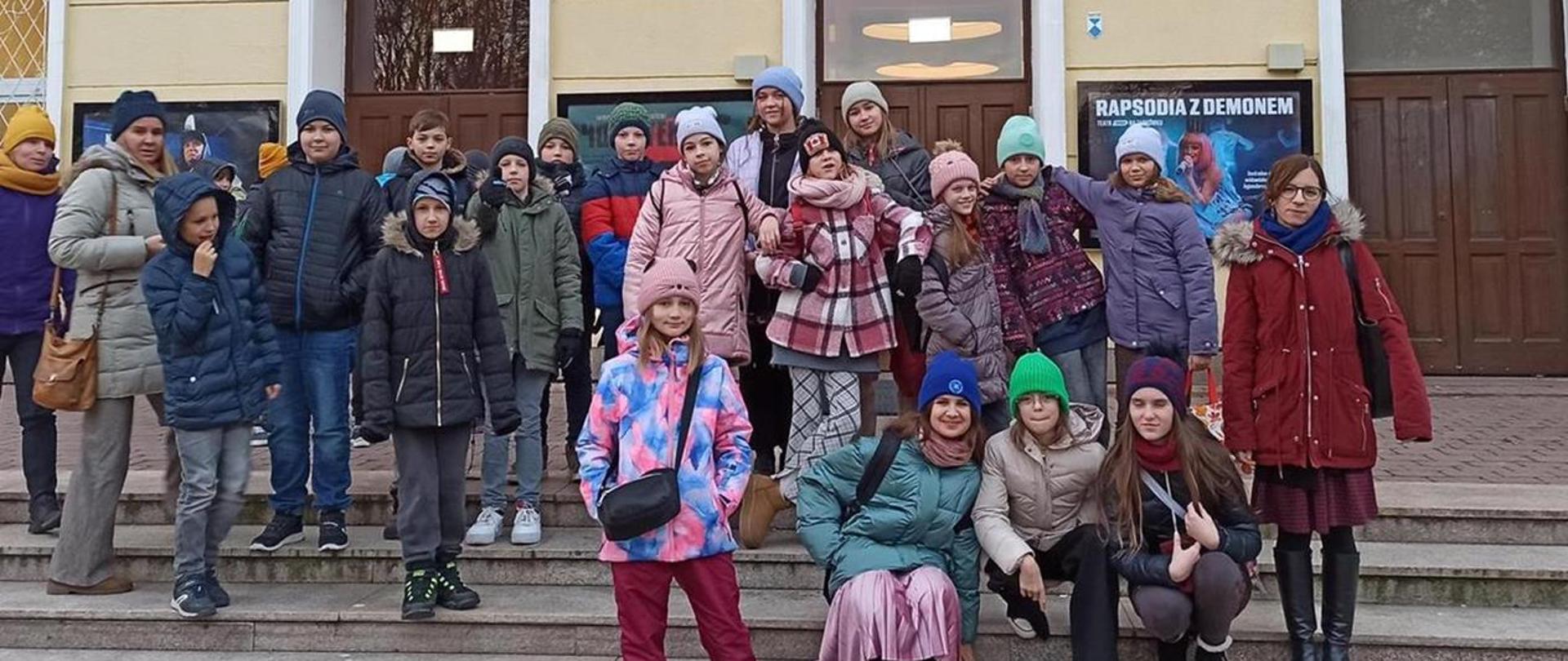 Dzieci z klasy 5 stoją przed teatrem 