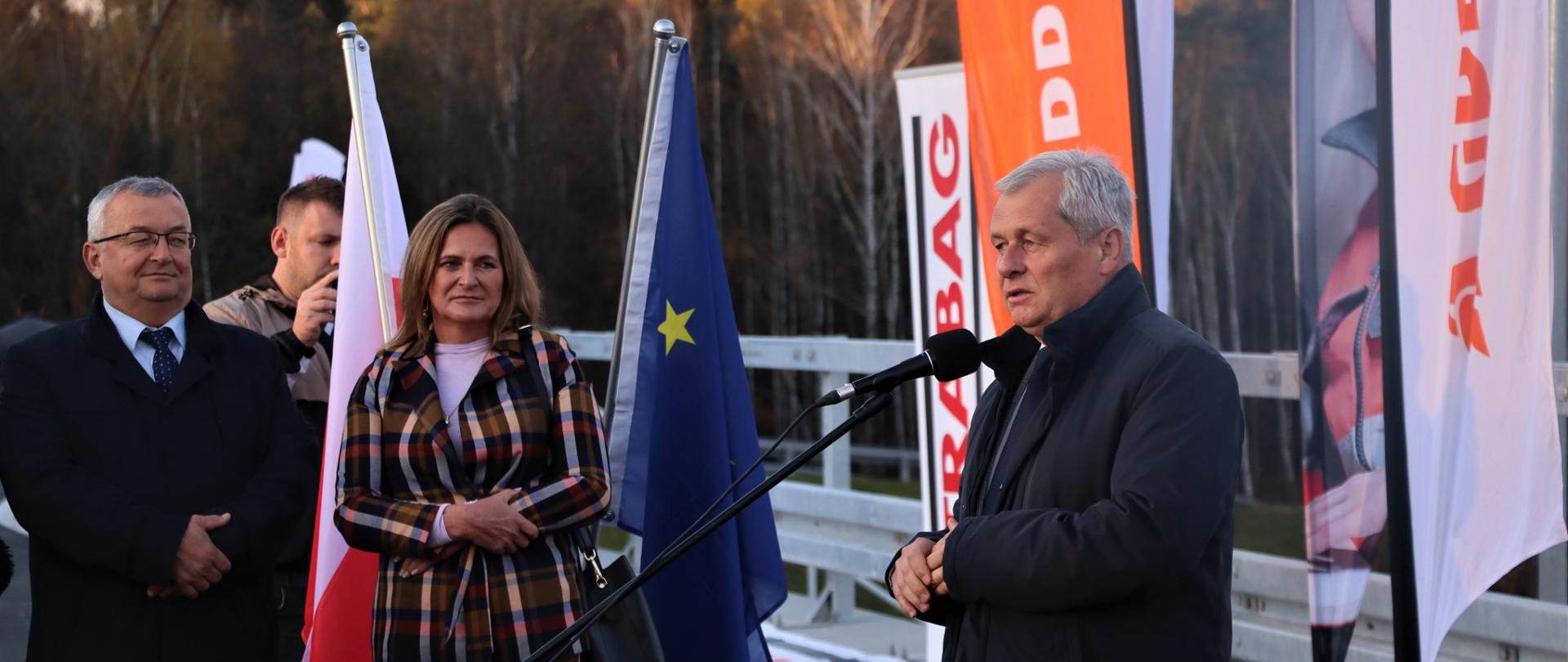 Przemawiający mężczyzna wśród ludzi, stojący na estakadzie nad obwodnicą