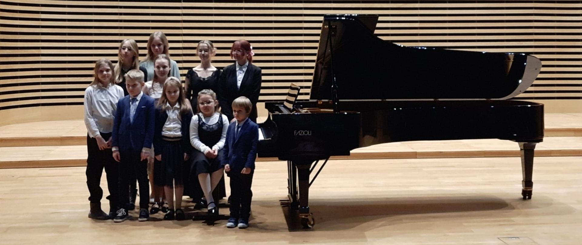 Grupa uczniów (10 osób) na scenie sali koncertowej PSM przy fortepianie