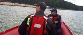 Na zdjęciu widzimy strażaka oraz policjanta, podczas patrolu na wodzie w łodzi. W tle widać jezioro.