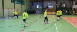 Zawodnicy rywalizujący podczas meczu futsalu w hali sportowej – strażacy piłkarze w jasnozielonych strojach podczas rozgrzewki przed meczem.