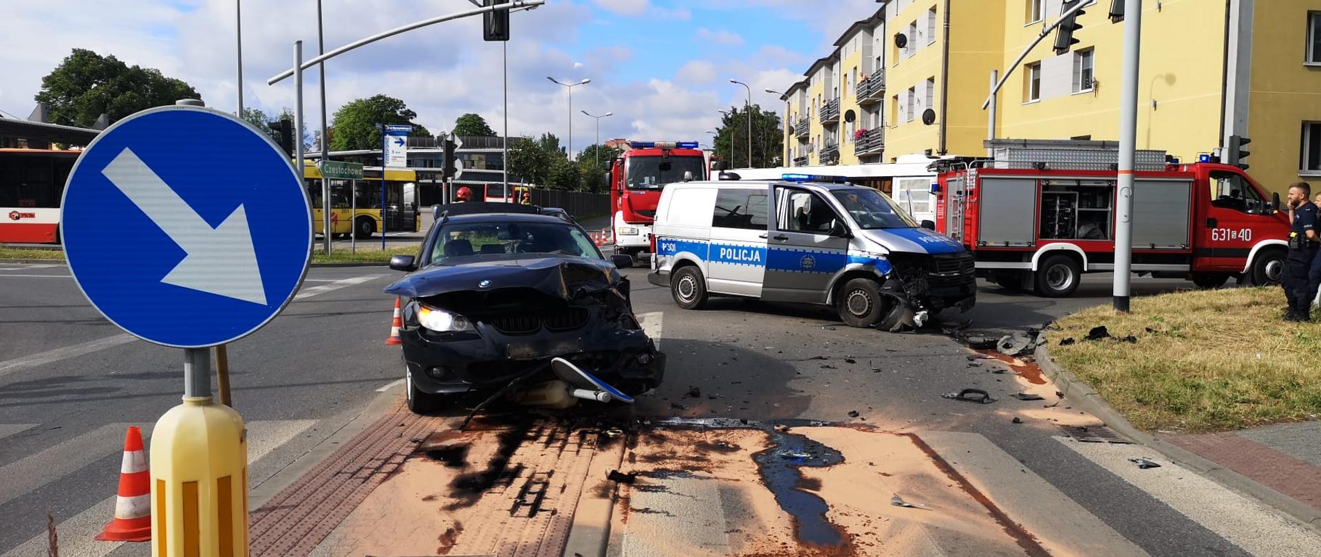 Rozbity samochód stoi przodem, obok rozbity radiowóz. W tle stoją wozy strażackie