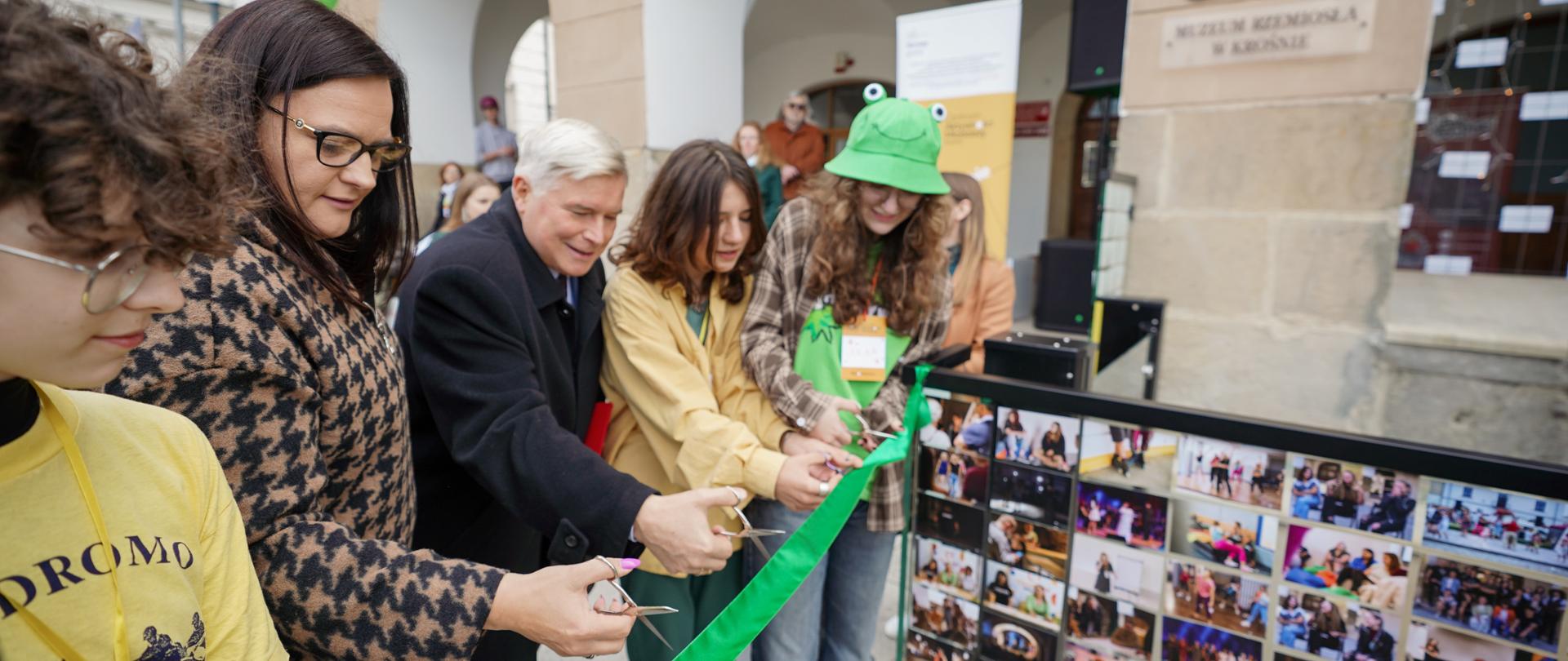 Grupa osób, w tym wiceminister Małgorzata Jarosińska-Jedynak przecinają wstęgę przed wejściem do budynku