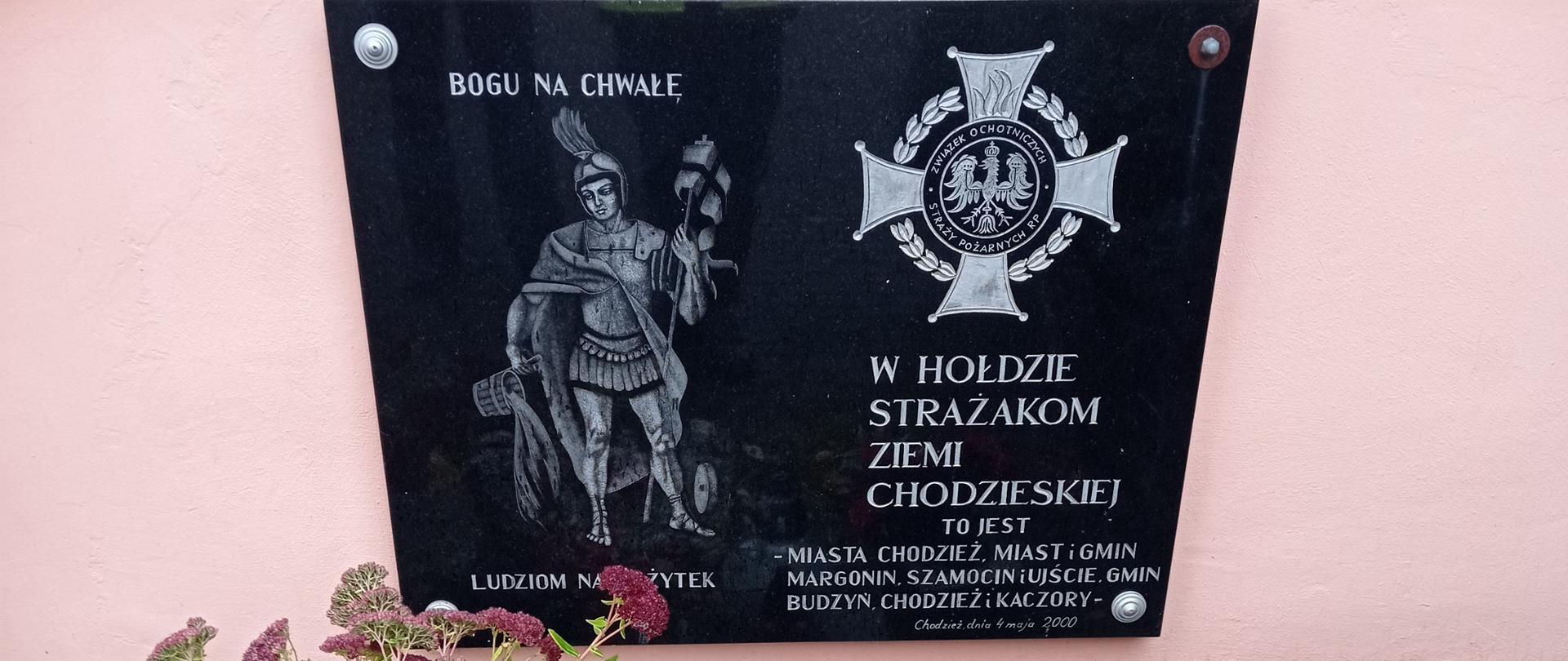 Zdjęcie przedstawia tablicę pamiątkową „W Hołdzie Strażakom Ziemi Chodzieskiej”.
W tle ściana.
