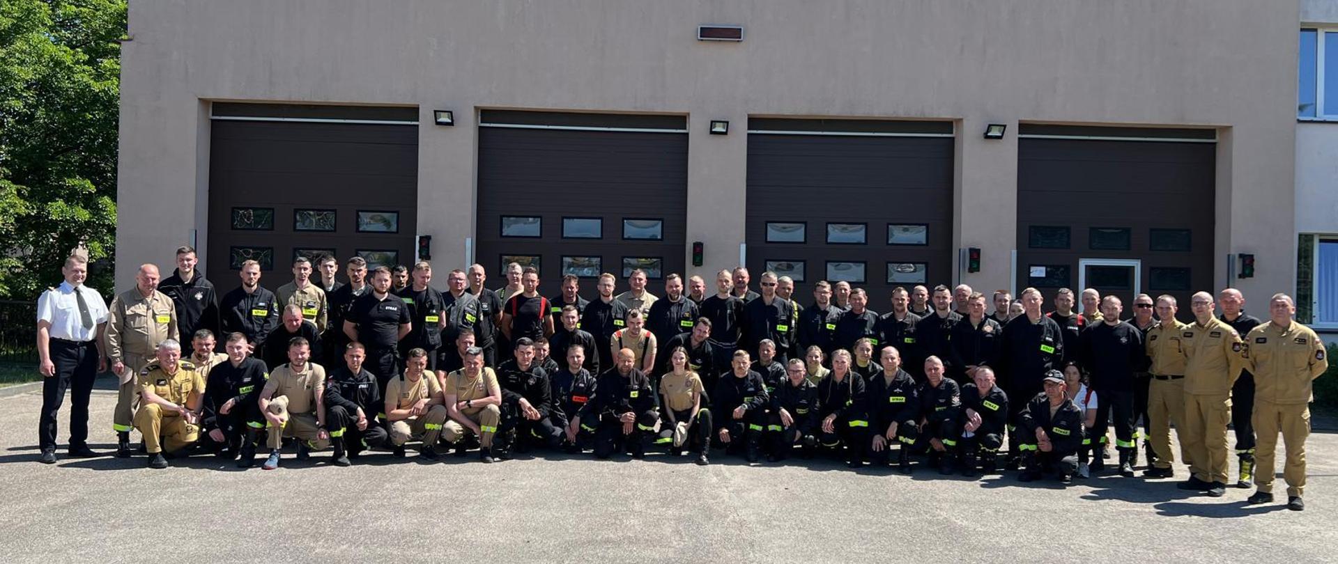 Zdjęcie przedstawia grupę strażaków ustawionych przed garażem Jednostki Ratowniczo-Gaśniczej nr 1 w Bytowie