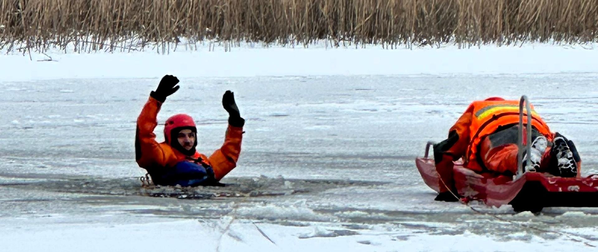 Jeden strażak udaje poszkodowanego w przeręblu, drugi strażak wraz z saniami lodowymi podejmuje próbę bezpiecznego uratowania pozoranta.