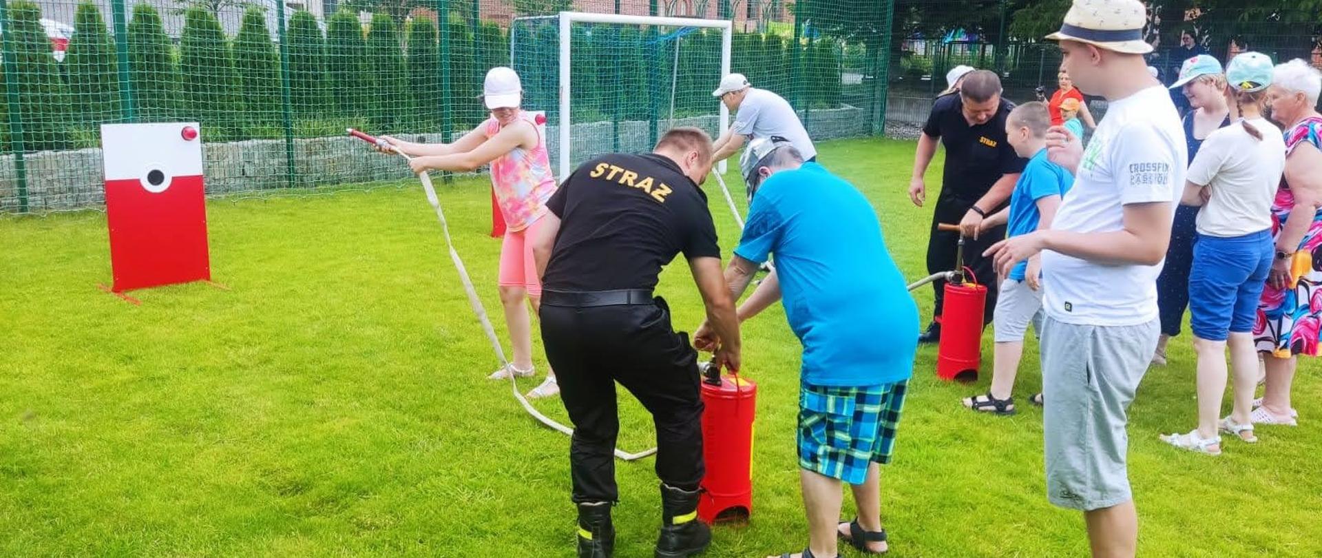 Na zdjęciu znajdują się funkcjonariusze z KP PSP w Chełmnie podczas pikniku z okazji rozpoczęcia wakacji. Piknik zorganizowano na terenie Domu Opieki Społecznej w Chełmnie. Zdjęcie wykonano na boisku wewnętrznym DPS-u.