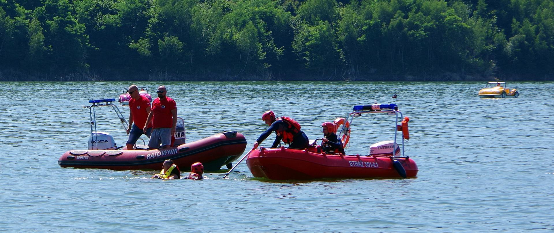 Dwie łodzie z ratownikami na jeziorze. Obok w wodzie ratownik i żeglarz podjęty z wody.