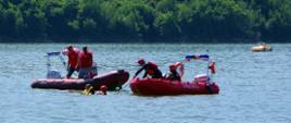 Dwie łodzie z ratownikami na jeziorze. Obok w wodzie ratownik i żeglarz podjęty z wody.