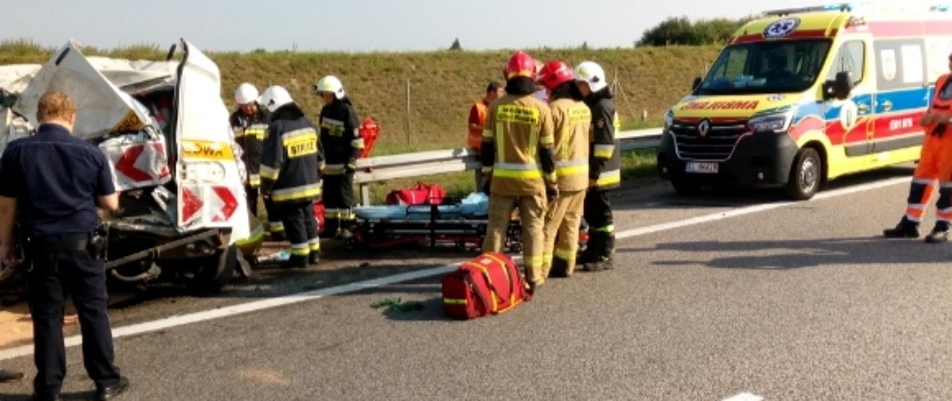 na zdjęciu strażacy zabezpieczają miejscu wypadku drogowego; po lewej stronie widoczne uszkodzone auto osobowe.