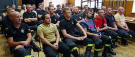 Widok z przodu. Zdjęcie zbiorowe strażaków OSP, którzy siedzą na sali szkoleniowej.