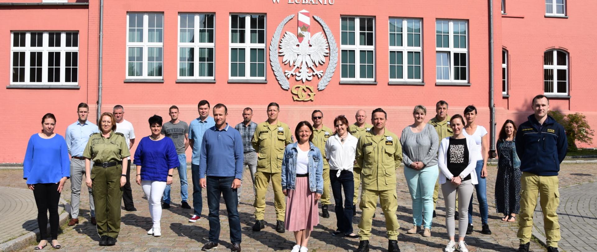 Stojąca grupa uczestników szkolenia dla członków grupy USAR Poland.W tle budynek Ośrodka Szkoleń Specjalistycznych Służby Granicznej. 