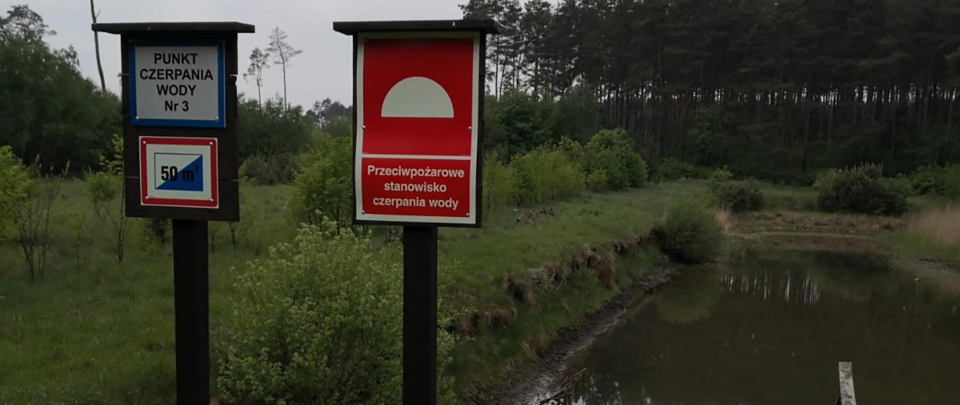 Zdjęcie przedstawia leśne punkty czerpania wody do celów przeciwpożarowych.
W tle drzewa i akwen wodny.
