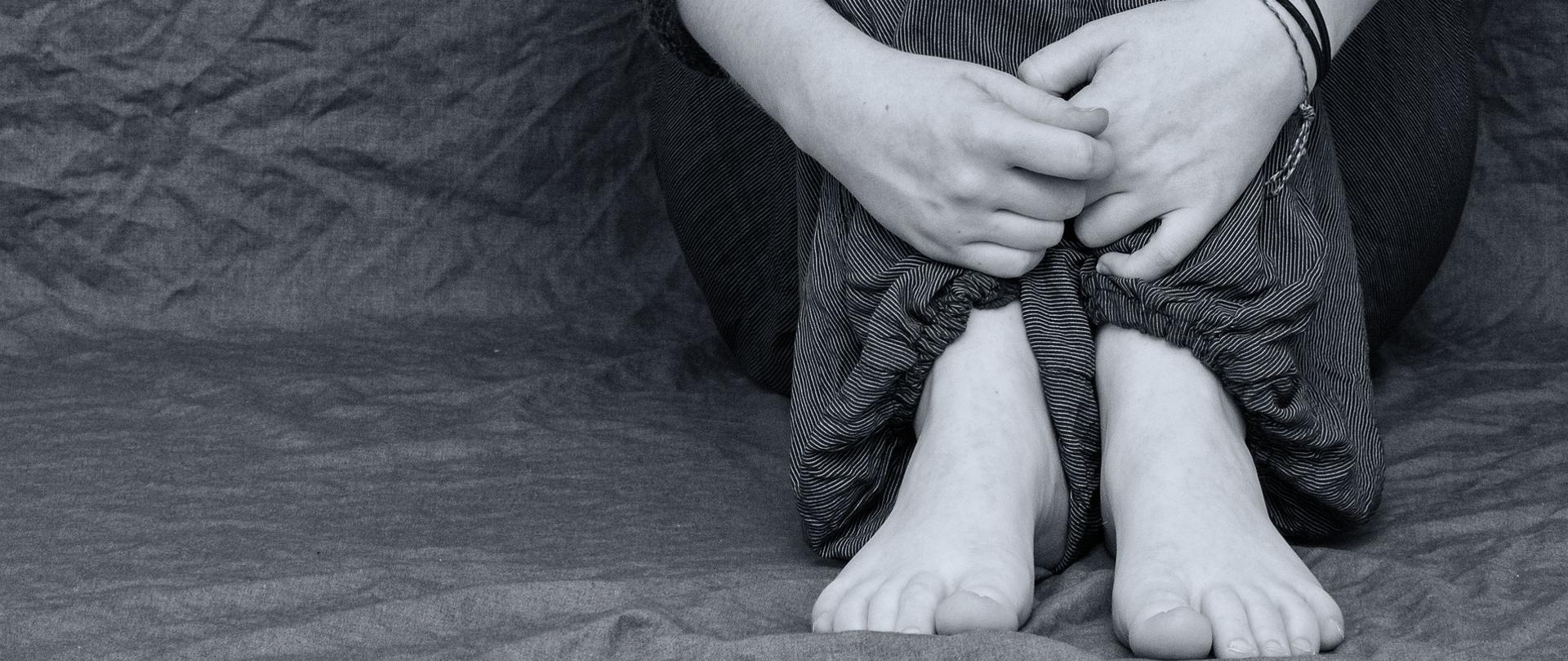 na zdjęciu widać bose stopy i obejmujące je ręce siedzącej skulonej osoby