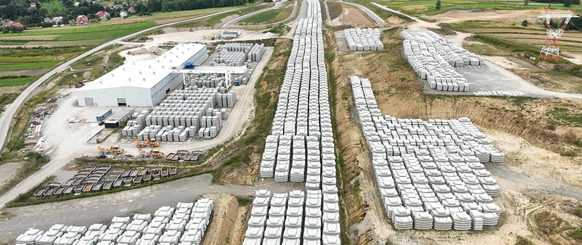 Hala prefabrykacji elementów obudowy tunelu po lewej stronie, widać także bardzo dużo już gotowych elementów ułożonych obok hali.