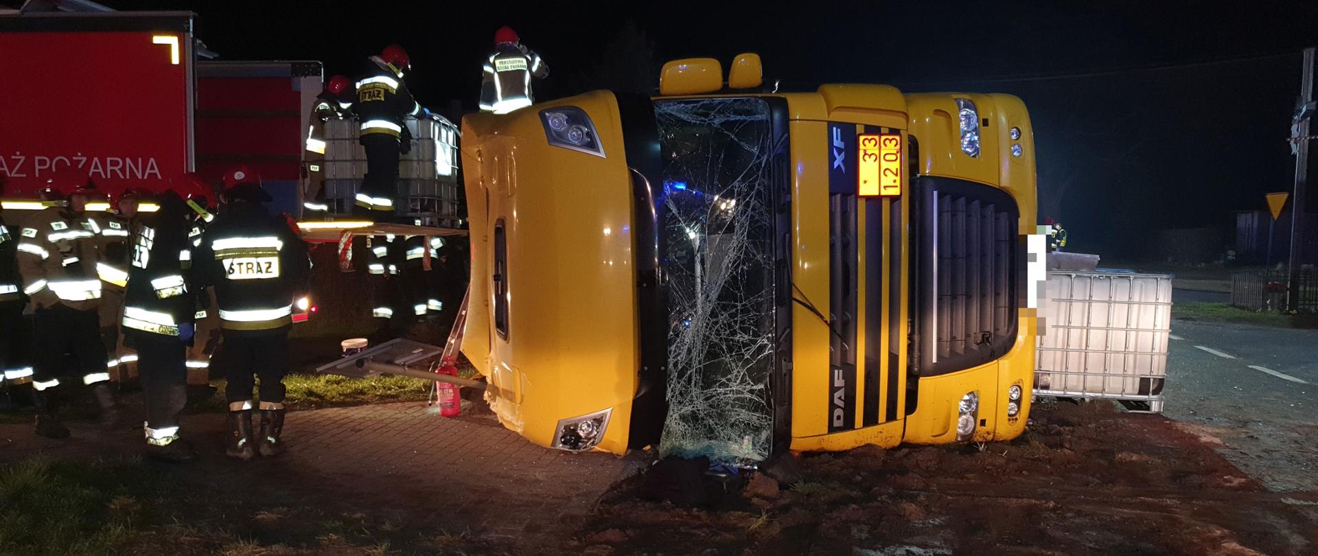 Zdjęcie przedstawia przód leżącej cysterny i przepompowywanie przez strażaków oleju napędowego.