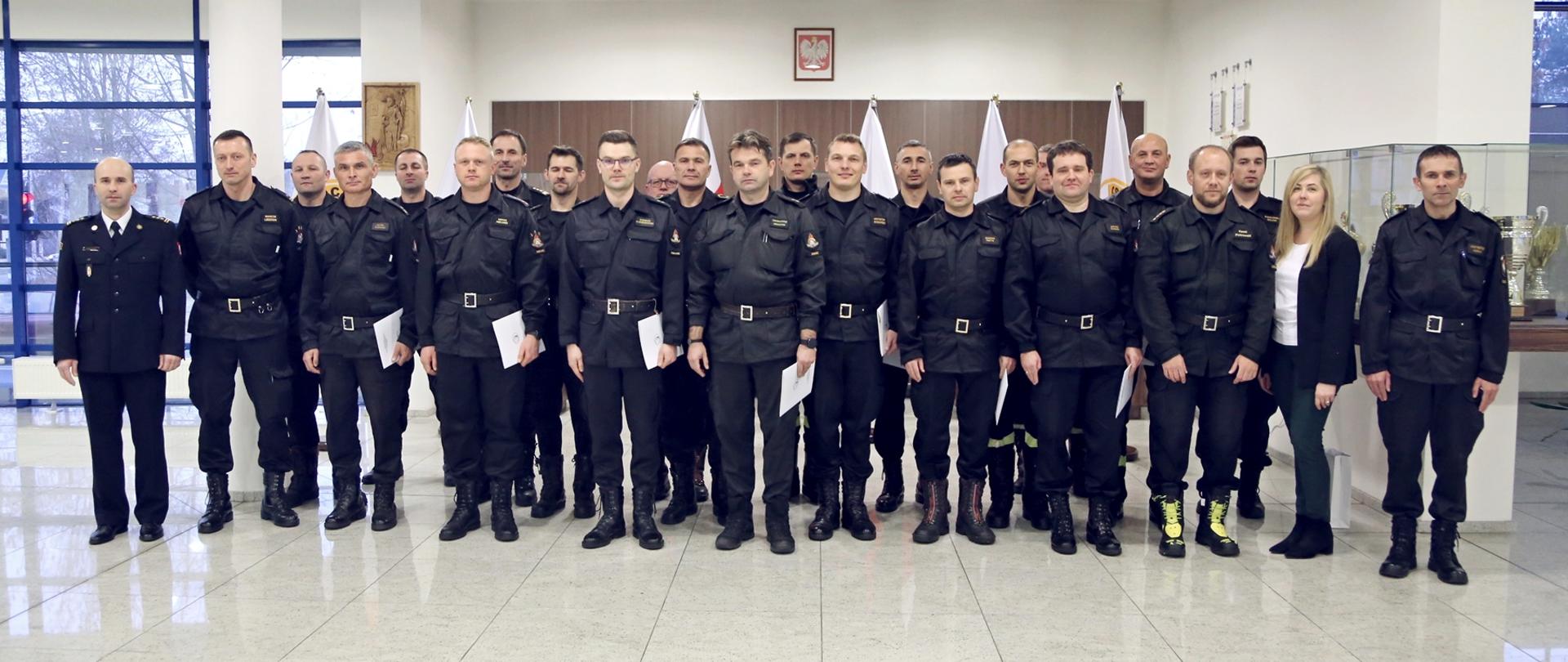 Grupowe zdjęcie uczestników szkolenia (20 funkcjonariuszy PSP) w towarzystwie Zastępcy Komendanta Centralnej Szkoły PSP oraz dwóch funkcjonariuszy CS PSP i kobiety