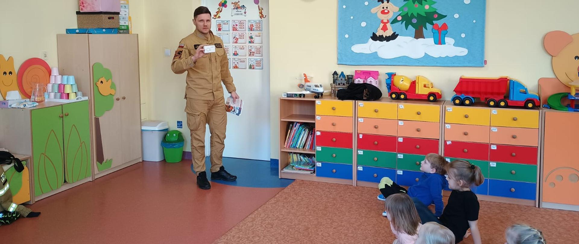 Funkcjonariusz KP PSP w Makowie Mazowieckim pokazuje dzieciom jak wygląda czujka dymu i tlenku węgla.